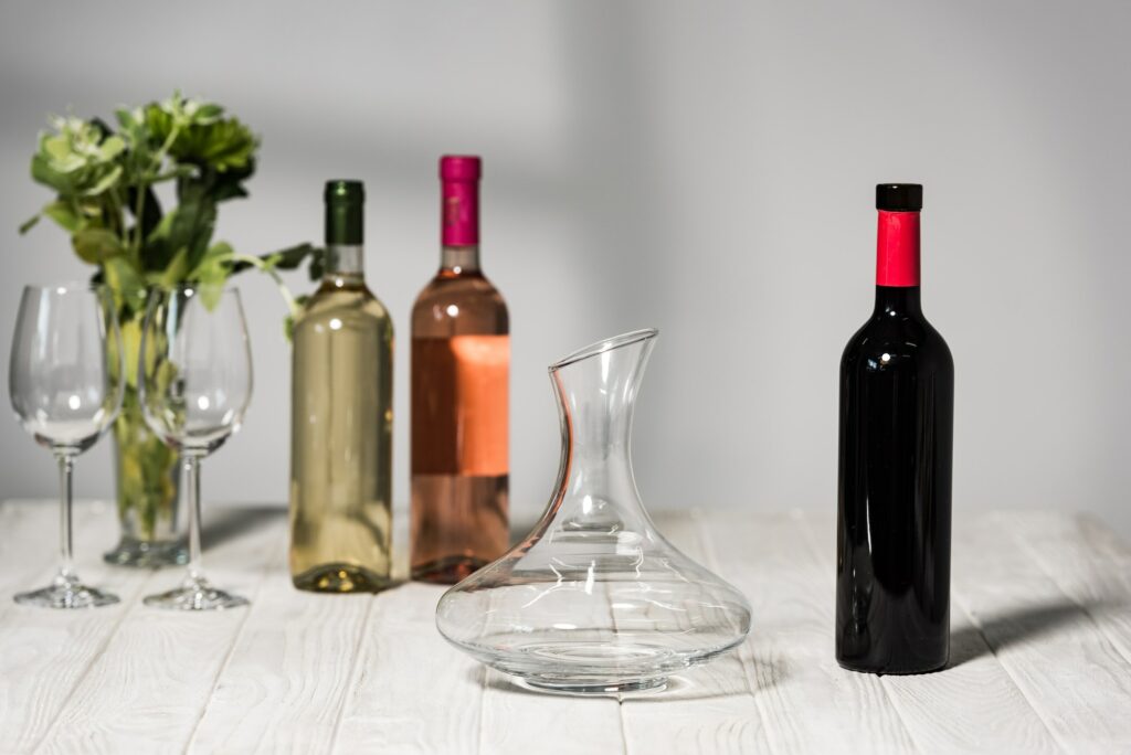 bottles of wine, wine glases, vase with green plants and jug on wooden surface